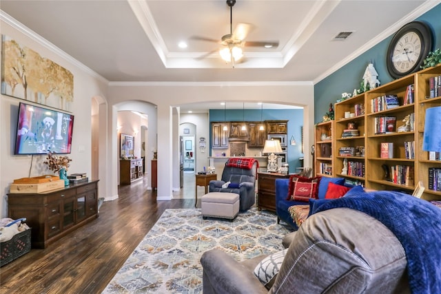 living room with crown molding, a raised ceiling, ceiling fan, and dark wood-type flooring