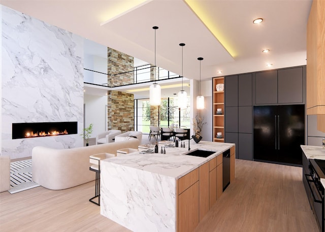 kitchen with light stone counters, light hardwood / wood-style flooring, pendant lighting, a center island with sink, and black appliances