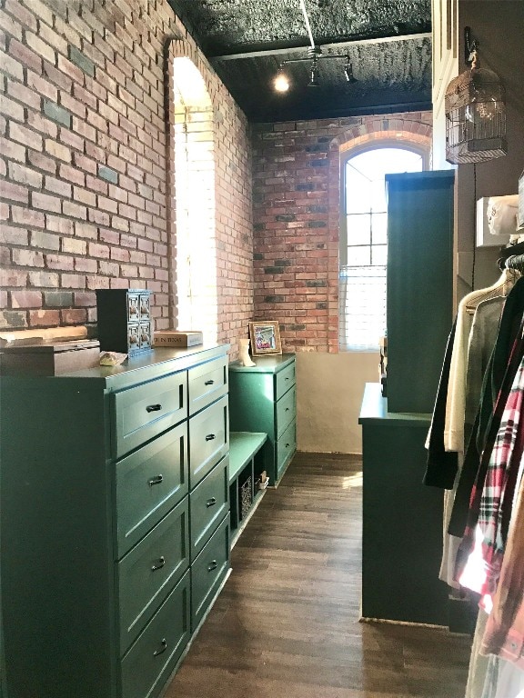 miscellaneous room featuring brick wall, dark wood-type flooring, and rail lighting