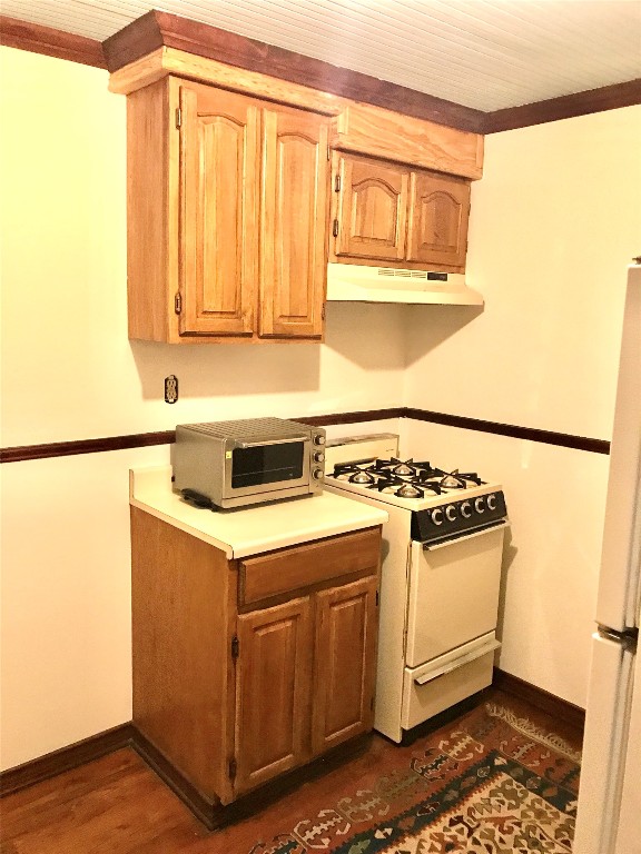 kitchen with ornamental molding, custom range hood, white appliances, and dark hardwood / wood-style flooring