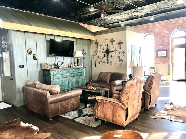 living room featuring dark hardwood / wood-style flooring, ceiling fan, and brick wall