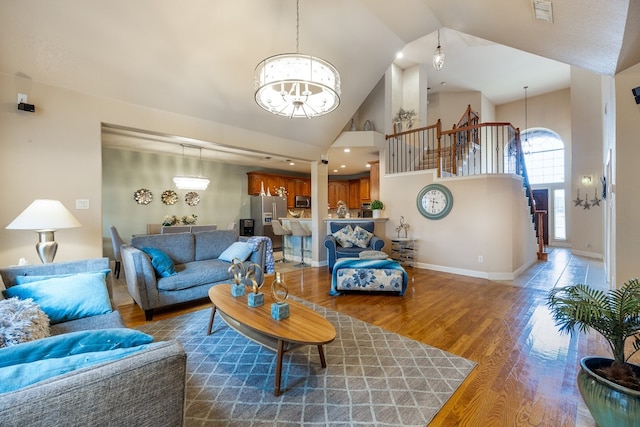 living room with hardwood / wood-style floors, a notable chandelier, and high vaulted ceiling