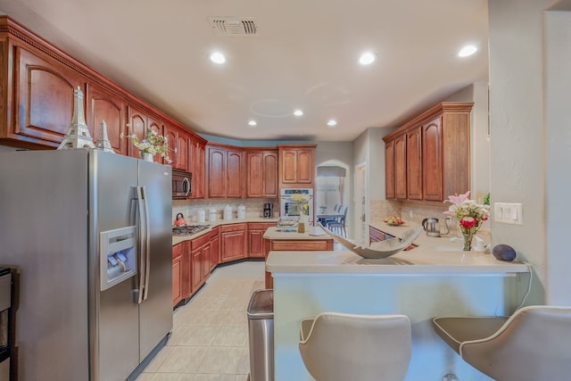 kitchen with stainless steel appliances, kitchen peninsula, light tile patterned floors, and backsplash