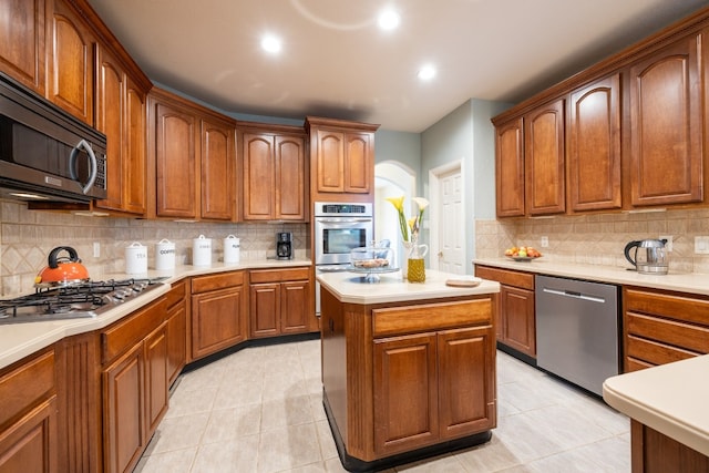 kitchen with decorative backsplash, a kitchen island, light tile patterned flooring, and appliances with stainless steel finishes