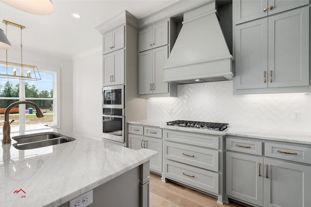 kitchen featuring appliances with stainless steel finishes, tasteful backsplash, custom range hood, light stone countertops, and sink