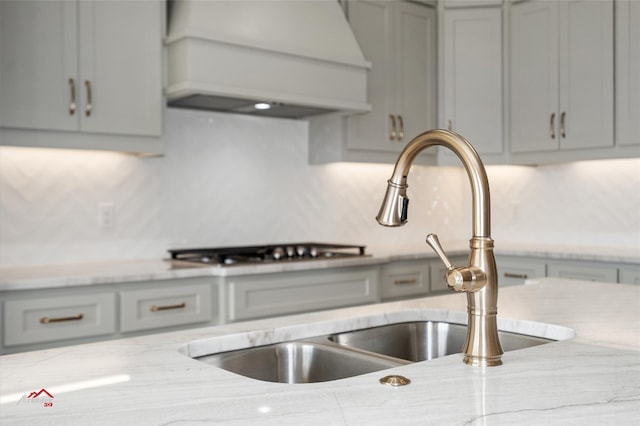 kitchen featuring light stone counters, gray cabinets, backsplash, custom range hood, and sink