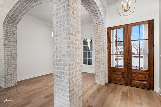 entrance foyer with a notable chandelier, brick wall, french doors, ornamental molding, and light hardwood / wood-style flooring