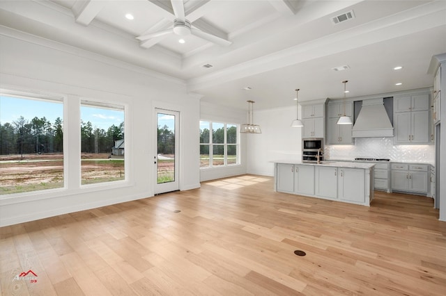 kitchen with light wood-type flooring, ceiling fan, coffered ceiling, decorative light fixtures, and custom exhaust hood