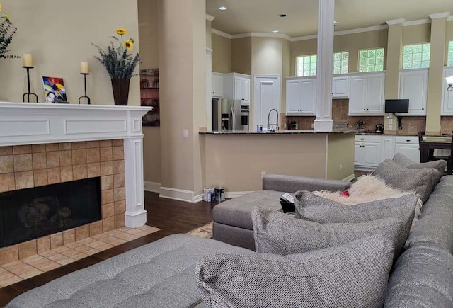 living room featuring crown molding, decorative columns, dark hardwood / wood-style floors, a tile fireplace, and sink