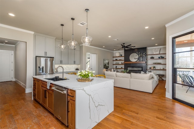 kitchen with light wood-type flooring, stainless steel appliances, white cabinets, a kitchen island with sink, and light stone counters