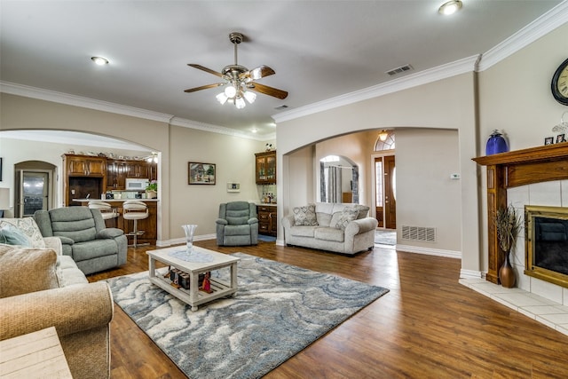 living room featuring a tile fireplace, ceiling fan, ornamental molding, and dark wood-type flooring