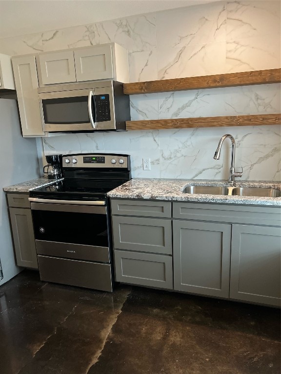 kitchen with gray cabinetry, light stone counters, appliances with stainless steel finishes, and sink