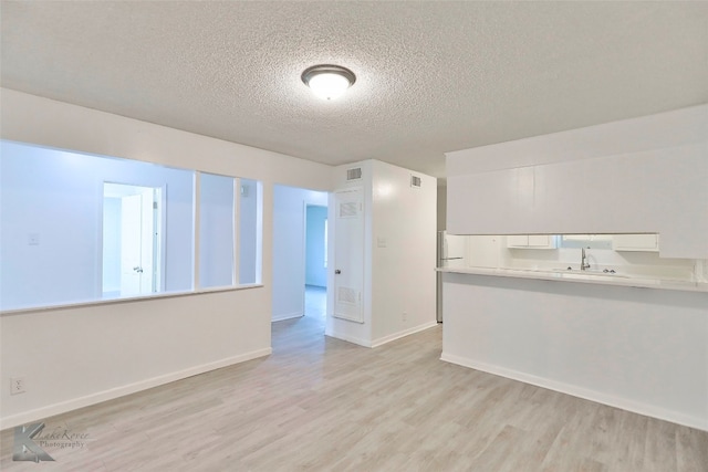 unfurnished room with a textured ceiling, sink, and light wood-type flooring