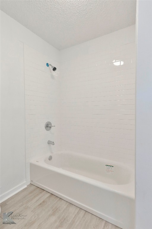 bathroom featuring tiled shower / bath combo, hardwood / wood-style flooring, and a textured ceiling