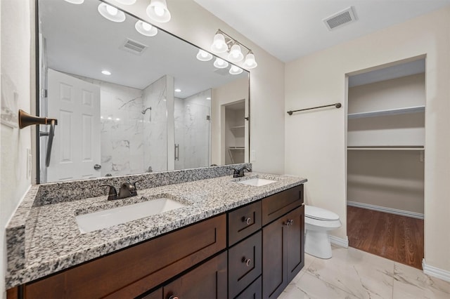 bathroom featuring toilet, oversized vanity, double sink, tiled shower, and hardwood / wood-style floors