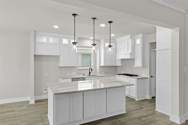 kitchen featuring pendant lighting, white cabinets, a center island, sink, and light stone counters