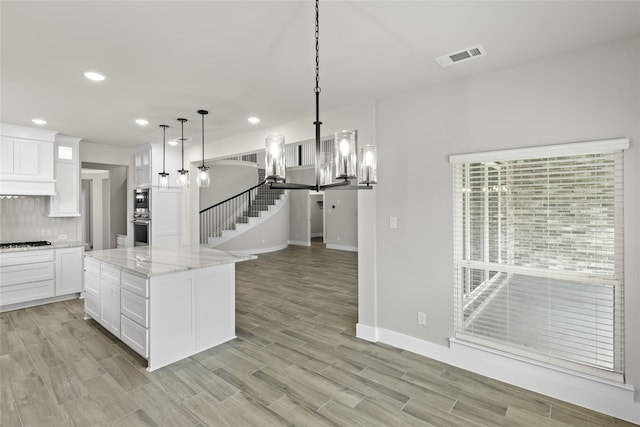 kitchen featuring white cabinetry, stainless steel appliances, tasteful backsplash, hanging light fixtures, and a center island