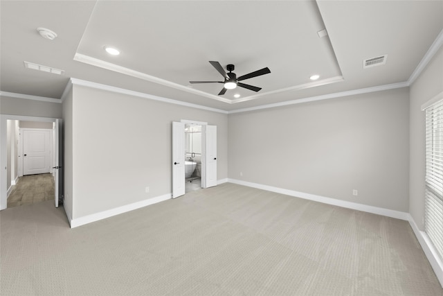 unfurnished bedroom featuring ensuite bathroom, ceiling fan, a raised ceiling, crown molding, and light carpet