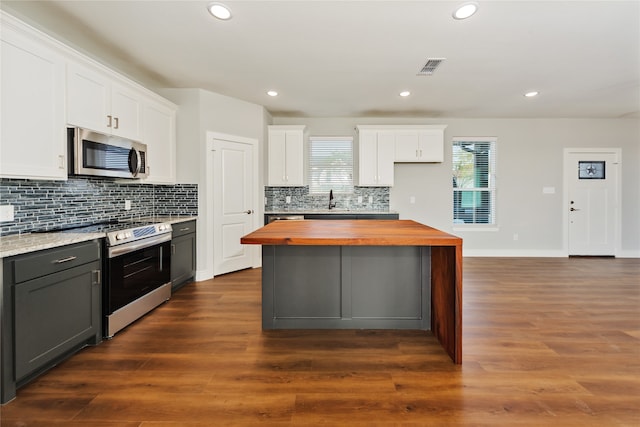 kitchen with appliances with stainless steel finishes, dark wood-type flooring, wood counters, and white cabinetry