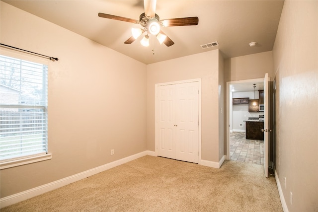 unfurnished bedroom featuring light carpet, a closet, and ceiling fan