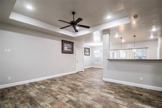 unfurnished living room featuring a tray ceiling, dark wood-type flooring, and ceiling fan with notable chandelier