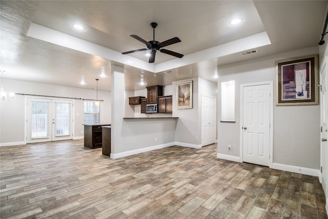 unfurnished living room with a raised ceiling, french doors, ceiling fan with notable chandelier, and hardwood / wood-style flooring