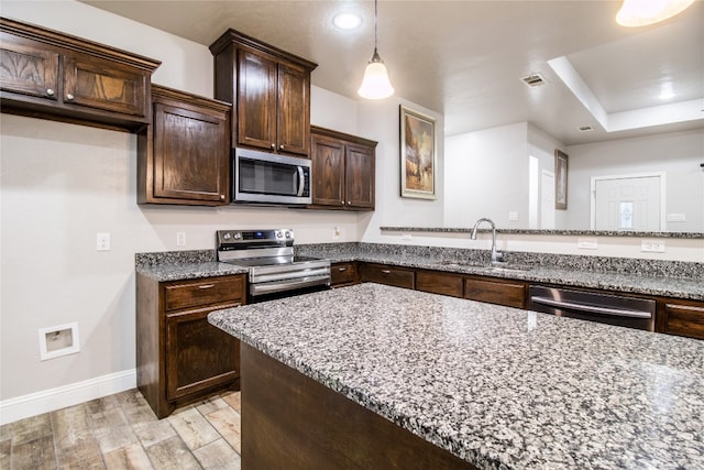 kitchen with stainless steel appliances, dark brown cabinets, light stone counters, and light hardwood / wood-style floors