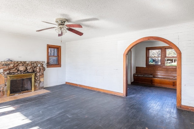 unfurnished living room with a textured ceiling, ceiling fan, dark hardwood / wood-style flooring, and a fireplace