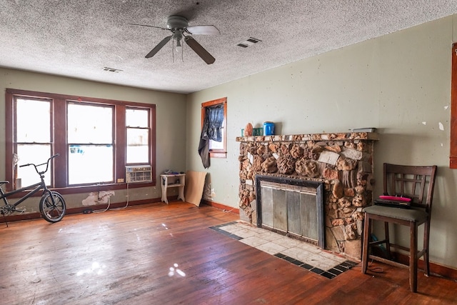 unfurnished living room with a textured ceiling, a stone fireplace, ceiling fan, and hardwood / wood-style flooring