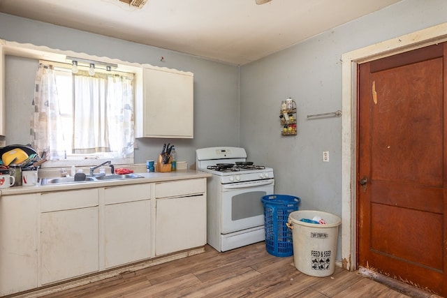 kitchen with white cabinets, light hardwood / wood-style flooring, white gas range oven, and sink