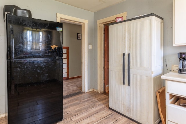 kitchen featuring light hardwood / wood-style flooring, white cabinetry, and black fridge