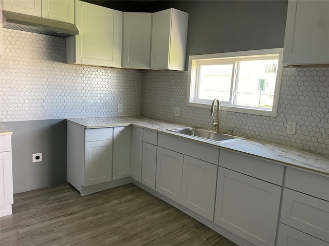 kitchen with tasteful backsplash, white cabinets, sink, and hardwood / wood-style flooring