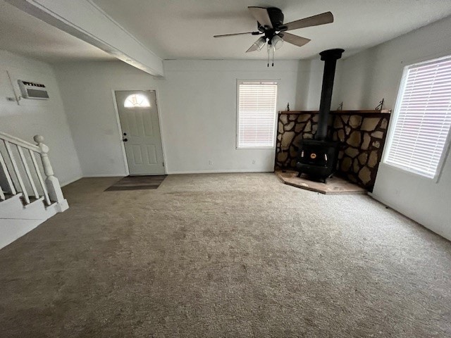 interior space featuring dark colored carpet, a wealth of natural light, ceiling fan, and a wood stove