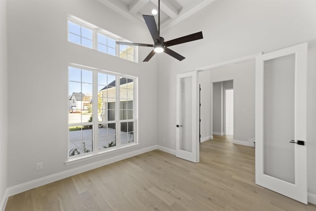 empty room with ceiling fan, beamed ceiling, high vaulted ceiling, and light wood-type flooring