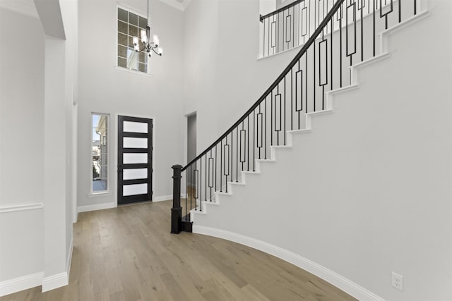 foyer entrance with a chandelier, a towering ceiling, hardwood / wood-style flooring, and ornamental molding