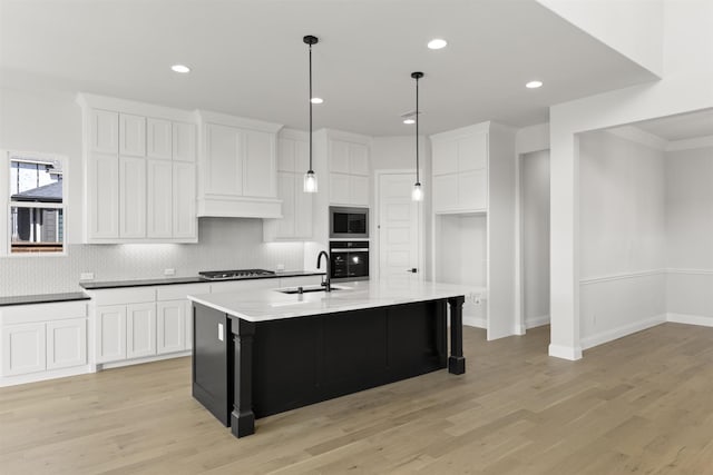 kitchen with white cabinets, appliances with stainless steel finishes, light wood-type flooring, and a center island with sink