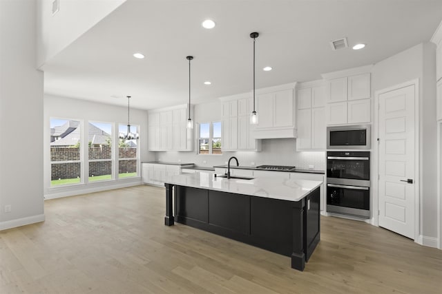 kitchen with sink, light hardwood / wood-style flooring, white cabinetry, and an island with sink