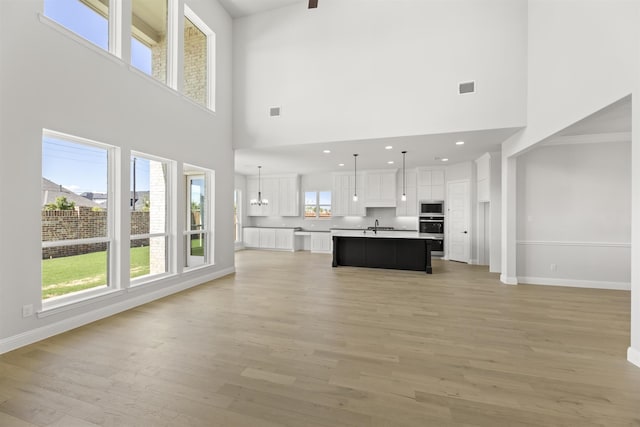 unfurnished living room with a chandelier, sink, light hardwood / wood-style floors, and a high ceiling