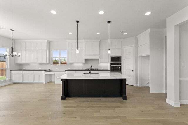 kitchen featuring black oven, stainless steel microwave, an island with sink, and a healthy amount of sunlight