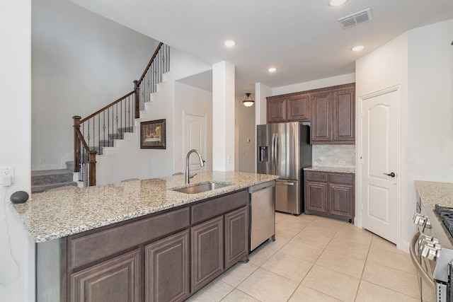 kitchen with stainless steel appliances, light tile floors, sink, and light stone counters