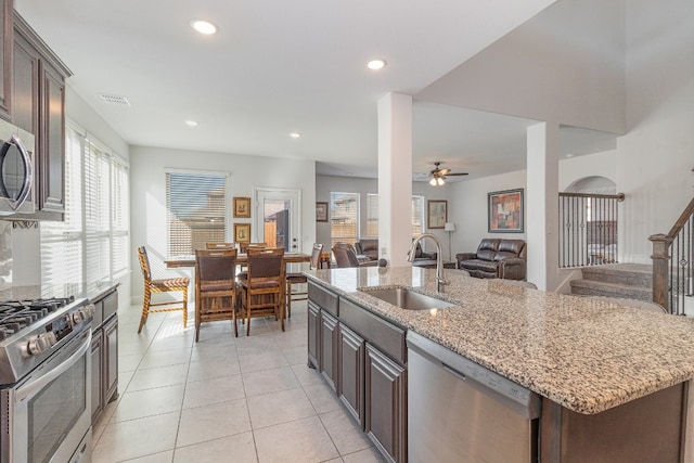 kitchen with ceiling fan, light stone countertops, appliances with stainless steel finishes, sink, and dark brown cabinetry