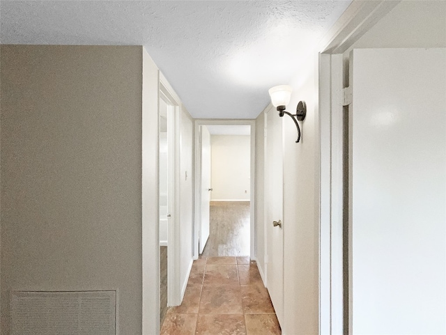 corridor featuring light tile flooring and a textured ceiling