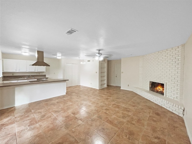 unfurnished living room featuring light tile flooring, brick wall, ceiling fan, and a fireplace