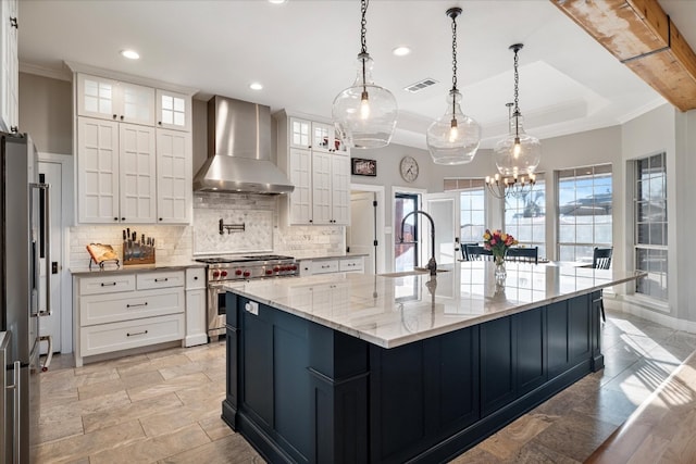 kitchen with wall chimney range hood, range with two ovens, a spacious island, pendant lighting, and white cabinets