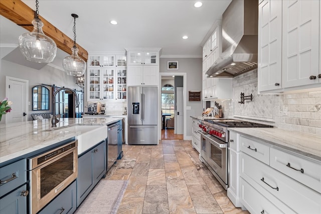 kitchen featuring wall chimney range hood, high quality appliances, backsplash, decorative light fixtures, and white cabinets