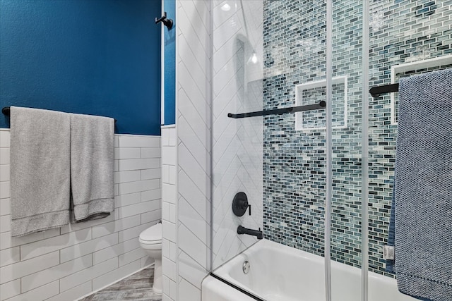 bathroom featuring toilet, combined bath / shower with glass door, and tile walls