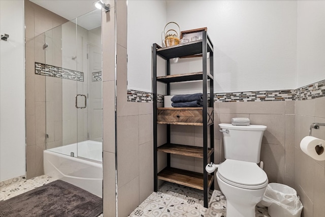 bathroom with tile walls, shower / bath combination with glass door, and toilet