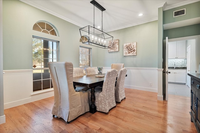 dining space with a chandelier, ornamental molding, sink, and light wood-type flooring