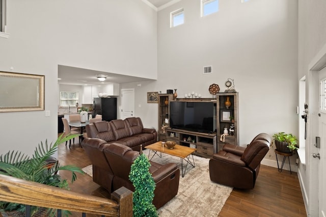 living room featuring plenty of natural light, ornamental molding, a towering ceiling, and dark hardwood / wood-style floors