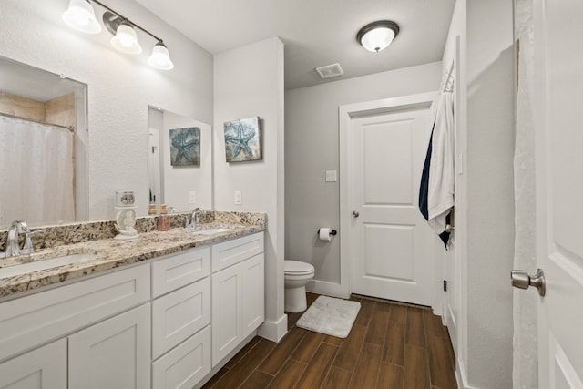 bathroom featuring toilet, dual bowl vanity, and wood-type flooring